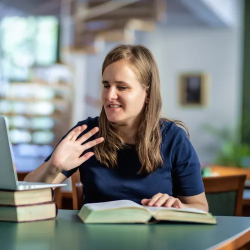 A visually impaired student studying at a library desk with a laptop and books.