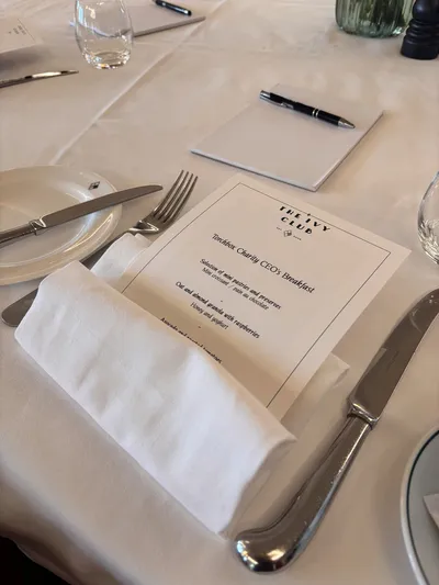 A neatly laid breakfast place setting at The Ivy Club, with a menu, folded white napkin, cutlery, notepad and pen.