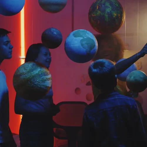 Children looking at a solar system display in a museum, lit in warm red and blue tones.