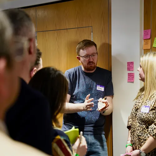 A person talking through ideas with a group of colleagues in front of a wall of sticky notes.