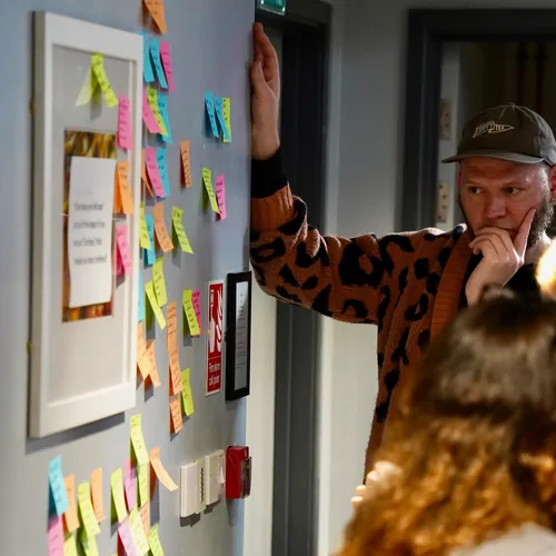 A person thoughtfully reviewing a wall covered in colourful sticky notes.