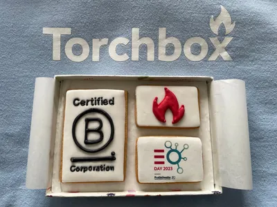 A box of iced biscuits featuring the B Corp logo, Torchbox flame icon and EO Day branding, placed on top of a Torchbox sweatshirt.