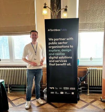 Mark standing beside a Torchbox Public banner. The banner reads: “Torchbox Public. We partner with public sector organisations to explore, design and realise digital solutions and services that benefit all.” Logos for organisations including Tate, FRC, NHS and London Museum appear at the bottom.
