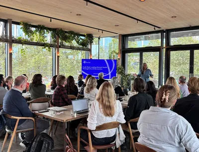Dr Sarah Hughes, CEO of Mind, speaks at the Charity Leaders’ Breakfast. She stands in front of a presentation screen while guests listen from round tables.