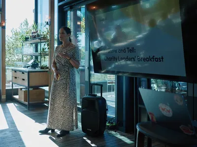 Lisa stands beside a presentation screen welcoming attendees to the AI Show and Tell: Charity Leaders’ Breakfast.