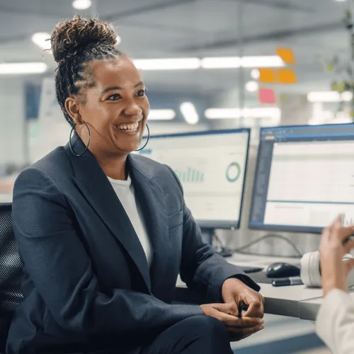 Two people chatting in an office in front of a computer.