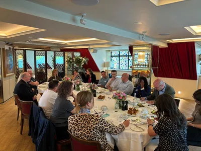 A group of charity leaders sit together around a large breakfast table at The Ivy Club, engaged in thoughtful conversation. The room is bright and welcoming, with floral arrangements, coffee cups and pastries on the table, while attendees listen, take notes and share ideas in an open, collaborative atmosphere.