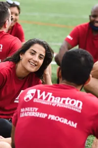 Young people sit together on field wearing red Wharton School University of Pennsylvania t-shirts