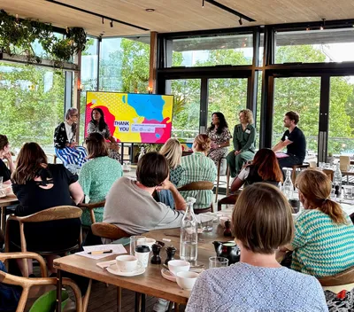 Charity professionals seated at tables listen to a panel of five speakers discussing how to engage younger supporters. The setting is bright and modern, with notepads and coffee cups on the tables.